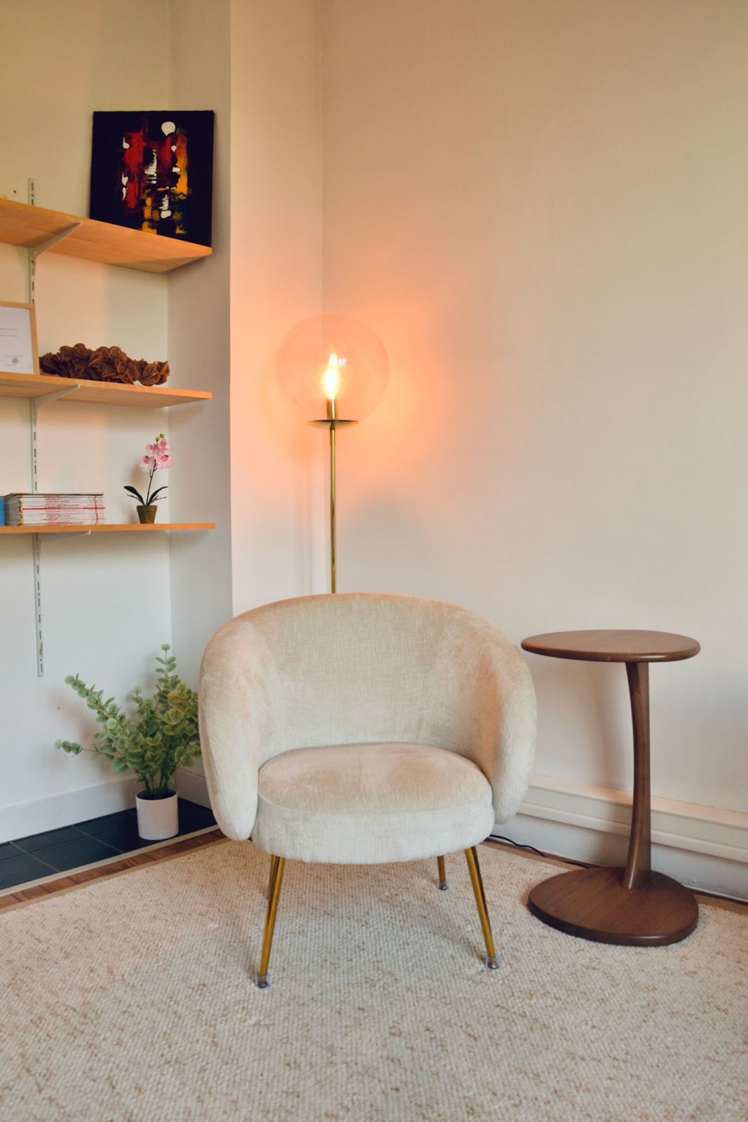 Le coin lecture du cabinet : le fauteuil, un guéridon, des étagères et le lampadaire allumé.